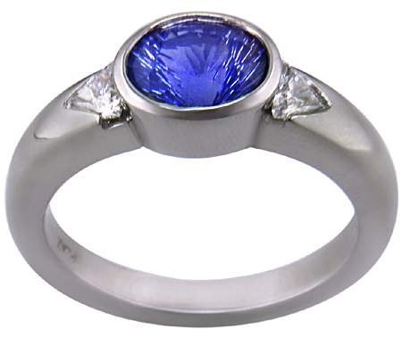 Side view of concave-faceted sapphire and trilliant diamonds in a custom platinum ring.