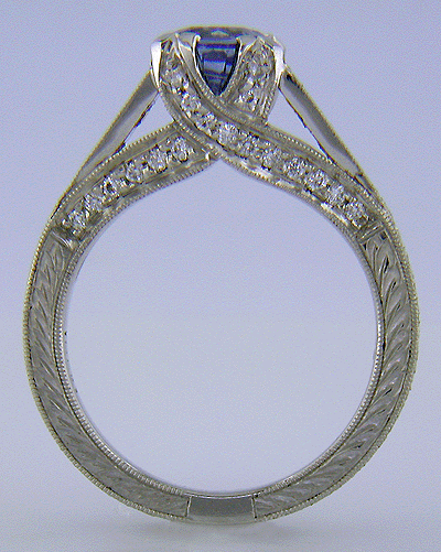 Side view of bright sapphire set with 42 accenting diamonds in an engraved platinum ring.