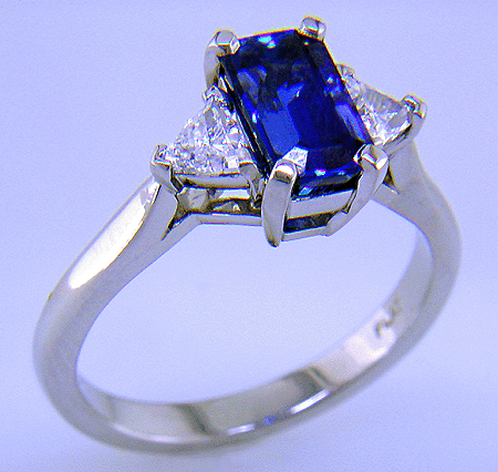 A hand-crafted platinum ring with a sriking emerald-cut sapphire and two sparkling trilliant diamonds.