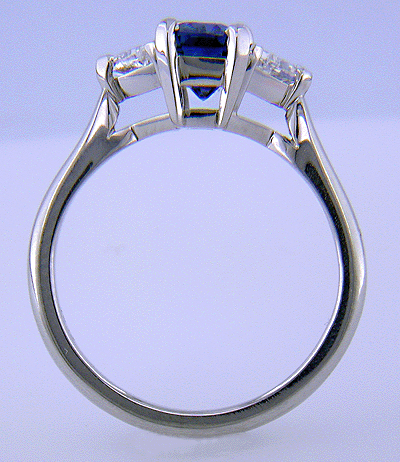 Side view of hand-crafted platinum ring with a sriking emerald-cut sapphire and two sparkling trilliant diamonds.