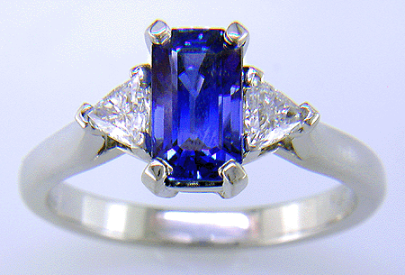 A handcrafted platinum ring with a sriking emerald-cut sapphire and two sparkling trilliant diamonds.