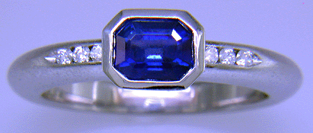 Emerald-cut sapphire set with round brilliant-cut diamonds in a custom platinum ring.