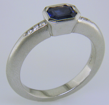 Emerald-cut sapphire set with round brilliant-cut diamonds in a custom platinum ring.